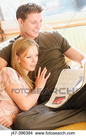 A young couple sitting reading the newspaper smiling View Large Photo Image Picture - A young couple sitting reading the newspaper smiling. Fotosearch