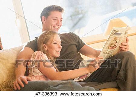 A young couple sitting reading the newspaper smiling View Large Photo Image Stock Image - A young couple sitting reading the newspaper smiling. Fotosearch