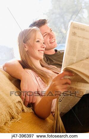 A young couple sitting reading the newspaper smiling View Large Photo Image Stock Photo - A young couple sitting reading the newspaper smiling. Fotosearch