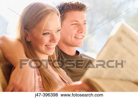 A young couple sitting reading the newspaper smiling, selective focus View Large Photo Image Stock Photo - A young couple sitting reading the newspaper smiling, selective focus. Fotosearch