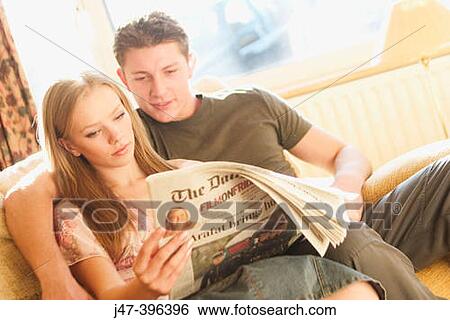 Stock Photograph - A young couple sitting reading the newspaper. Fotosearch