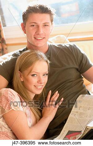 A young couple sitting reading the newspaper smiling into camera View Large Photo Image Stock Photography - A young couple sitting reading the newspaper smiling into camera. Fotosearch