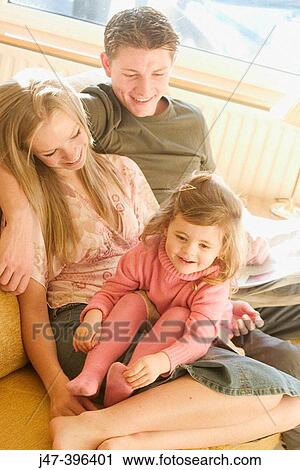 Stock Image - A young couple sitting together with a 3 year old gir on her knee all smiling. Fotosearch