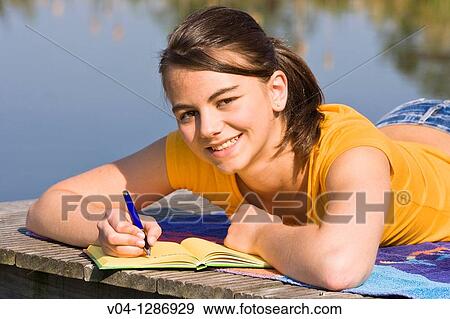 Stock Photo - A young girl writing into her diary at a lake, smiling at the camera.. Fotosearch