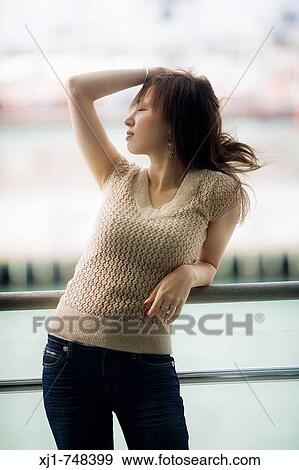 Stock Photo - A young Japanese woman leans against a deck railing outside her hotel room. Fotosearch