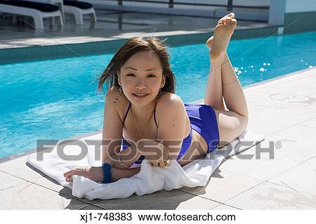 Stock Image - A young Japanese woman lying on a towell beside a hotel complex swimming pool.. Fotosearch