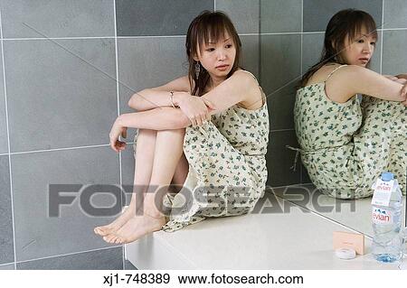 Stock Photo - A young Japanese woman sits on a hotel bathroom vanity unit.. Fotosearch