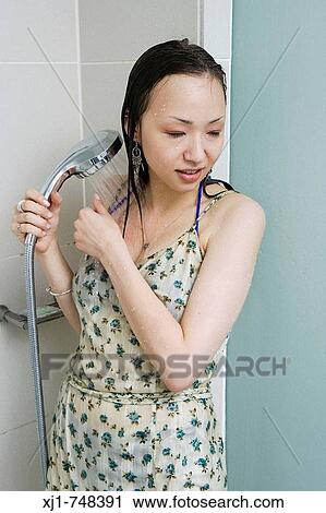 Stock Image - A young Japanese woman stands in a shower while wearing a dress.. Fotosearch