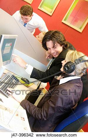 A young man and lady at work on a computer, she's wearing headphones, hes standing and pointing at the screen smiling View Large Photo Image Stock Image - A young man and lady at work on a computer, she's wearing headphones, hes standing and pointing at the screen smiling. Fotosearch