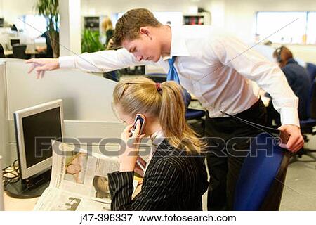 Stock Photo - A young man and lady in suits, sitting at a computer, looking at the newspaper and on a mobile phone. Fotosearch