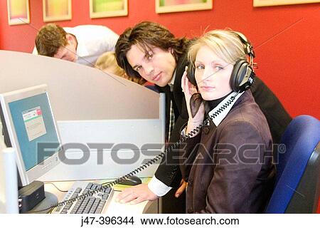 Picture - A young man and lady in suits, working at a computer, looking into camera. Fotosearch
