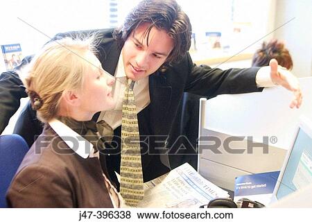 Stock Photo - A young man and lady in suits, working at a computer, talking. Fotosearch
