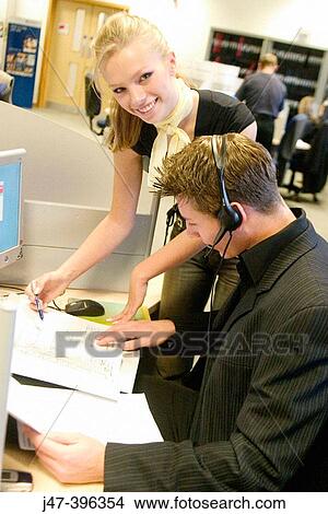 Picture - A young man and lady sitting at a computer, looking at papers working. Fotosearch
