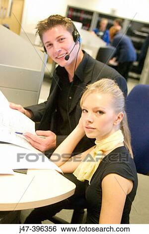 A young man and lady sitting at a computer, looking at papers smiling into camera View Large Photo Image Stock Photograph - A young man and lady sitting at a computer, looking at papers smiling into camera. Fotosearch