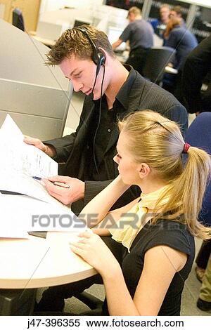 Stock Photography - A young man and lady sitting at a computer, looking at papers working. Fotosearch