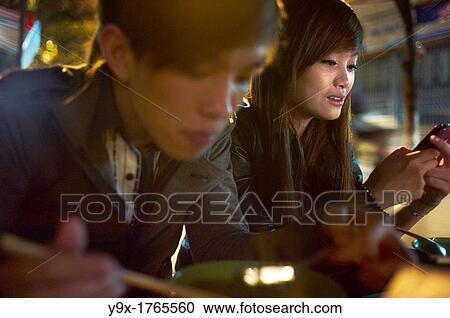 A young man eating and a woman on her cellphone at night View Large Photo Image Stock Image - A young man eating and a woman on her cellphone at night. Fotosearch