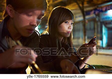 A young man eating and a woman on her cellphone at night View Large Photo Image Stock Photo - A young man eating and a woman on her cellphone at night. Fotosearch
