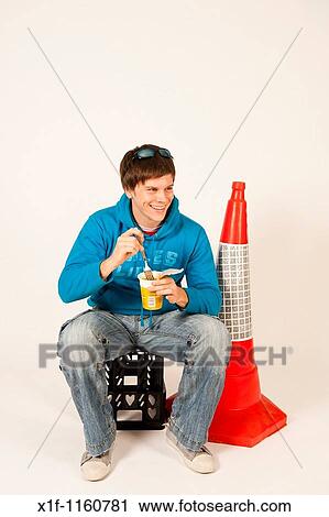 A young man eating pot noodle hot snack sitting on a plastic crate next to an orange traffic cone, UK View Large Photo Image Stock Image - A young man eating pot noodle hot snack sitting on a plastic crate next to an orange traffic cone, UK. Fotosearch