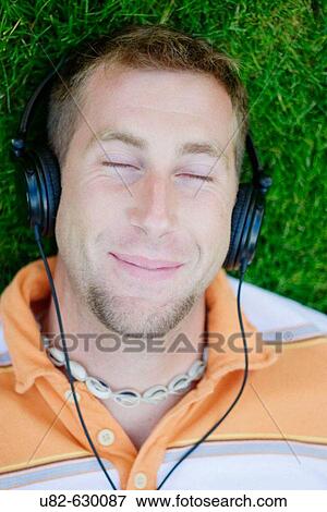 A young man laying on grass while listening to music on his headphones View Large Photo Image Stock Photo - A young man laying on grass while listening to music on his headphones. Fotosearch