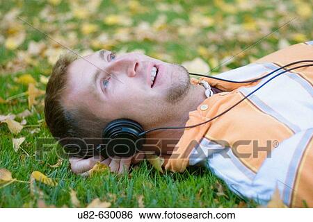 A young man laying on grass while listening to music on his headphones View Large Photo Image Stock Photograph - A young man laying on grass while listening to music on his headphones. Fotosearch