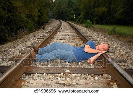 A young man lies down across a railroad track. He is in a very dangerous position, and seems suicidal. View Large Photo Image Stock Photograph - A young man lies down across a railroad track. He is in a very dangerous position, and seems suicidal.. Fotosearch
