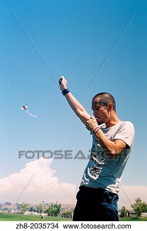 Picture - A young man lights a cigarette while flying a bee shaped kite at a Los Angeles State Historic Park just outside of downtown Los Angeles.. Fotosearch