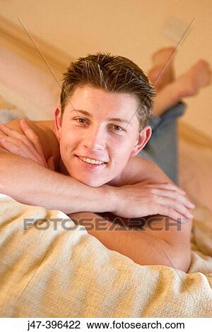 Stock Image - A young man lying on a bed looking into camera smiling. Fotosearch
