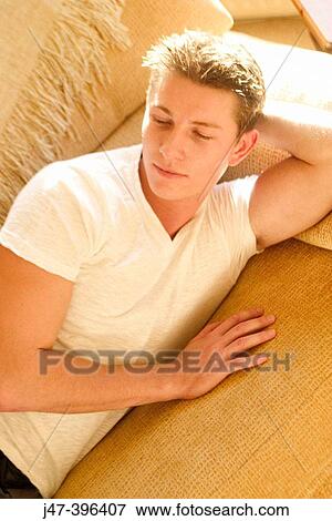A young man lying on a sofa looking off camera View Large Photo Image Stock Photo - A young man lying on a sofa looking off camera. Fotosearch