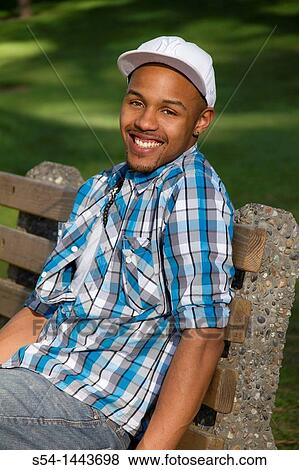 A young man sitting on a bench at a park. View Large Photo Image Stock Photo - A young man sitting on a bench at a park.. Fotosearch