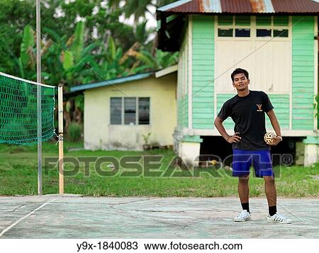 Stock Image - A young man standing and holding a rattan ball that is used in the sport Sepak takraw, a type of kick volleyball native to the Malay-Thai Peninsula. Fotosearch