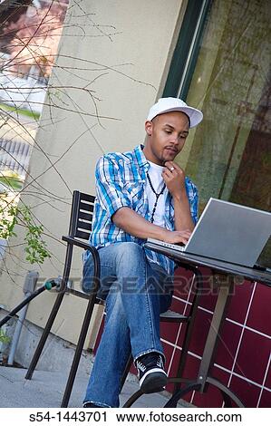 Stock Image - A young man studying outdoors on a laptop.. Fotosearch