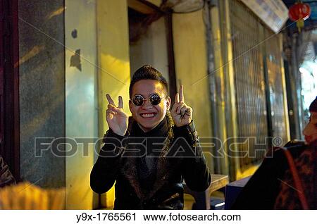A young man with sunglasses poses with victory signs at an outdoor restaurant while a young woman looks on View Large Photo Image Stock Image - A young man with sunglasses poses with victory signs at an outdoor restaurant while a young woman looks on. Fotosearch