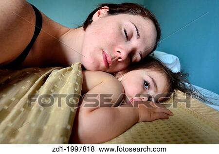 Stock Photo - A young mother hugs her baby in bed.. Fotosearch