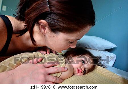 Stock Photograph - A young mother hugs her baby in bed.. Fotosearch