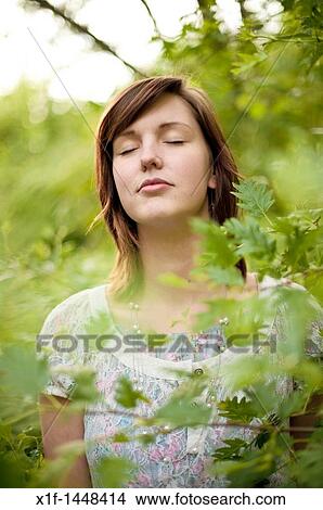 Picture - A young slim attractive girl in her late teens or early 20? s, outdoors in a woodland glade with her eyes closed, UK. Fotosearch