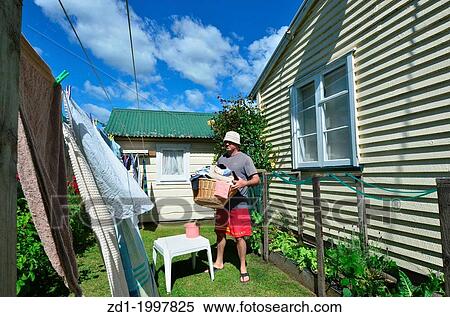 Stock Photography - A young smiling man drinks beer while hanging clothes on clothes line using clothes peg.. Fotosearch