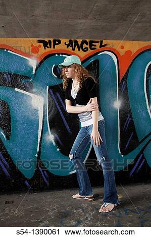 Stock Image - A young woman by a wall covered with graffiti. Fotosearch