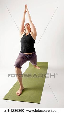 Stock Image - A young woman doing yoga on a green mat. Fotosearch