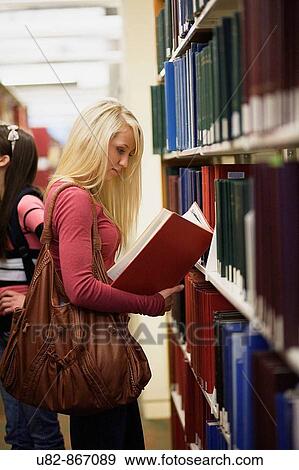 A young woman examines a book in a library aisle View Large Photo Image Stock Photo - A young woman examines a book in a library aisle. Fotosearch