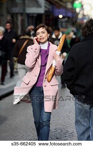 Stock Photography - A young woman holding a baguette and talking on her cell phone on the street of Paris. Paris. France.. Fotosearch