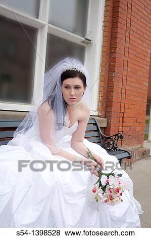 Stock Photo - A young woman in a bridal gown, crying and sitting on a bench by city hall in Rosalia, Washington, USA.. Fotosearch