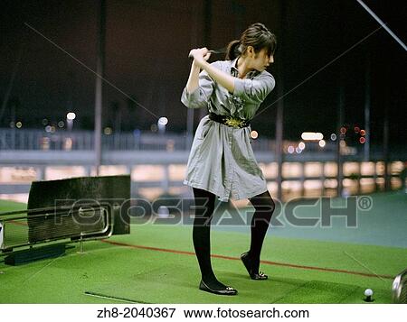 Stock Photo - A young woman in a dress playing golf at a driving range in Korea Town, Los Angeles.. Fotosearch