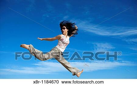 Stock Image - A young woman jumps in Australia beach againts a blue sky.. Fotosearch