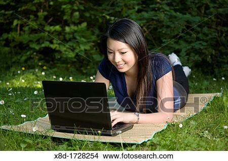 A young woman laying on a mat while using a wireless laptop in a park View Large Photo Image Picture - A young woman laying on a mat while using a wireless laptop in a park. Fotosearch