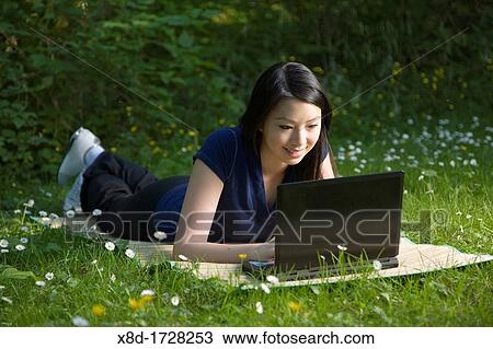 A young woman laying on a mat while using a wireless laptop in a park View Large Photo Image Stock Image - A young woman laying on a mat while using a wireless laptop in a park. Fotosearch