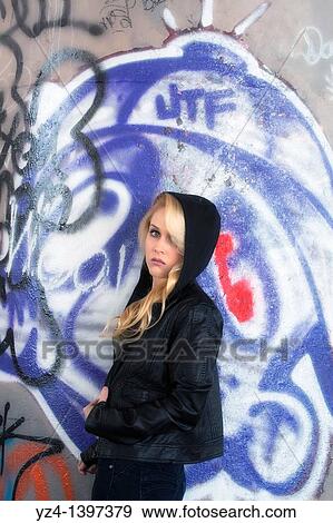 Stock Photo - A young woman leaning against a wall covered with graffiti.. Fotosearch