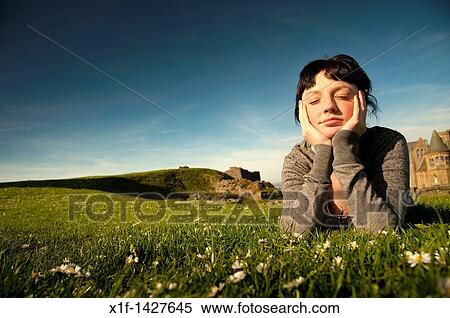 A young woman lying on the grass outdoors with her head in her hands daydreaming on a spring summer afternoon UK View Large Photo Image Stock Photography - A young woman lying on the grass outdoors with her head in her hands daydreaming on a spring summer afternoon UK. Fotosearch