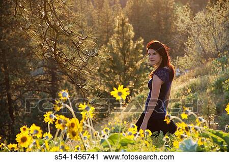 Stock Image - A young woman outdoors in the spring, in a field of Balsamroot flowers.. Fotosearch
