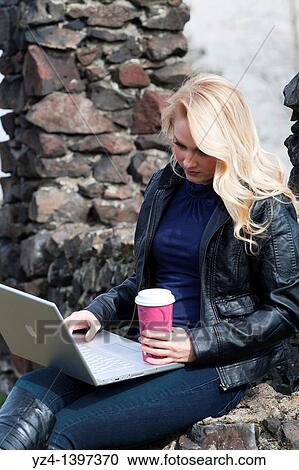 Stock Image - A young woman outdoors with a laptop and coffee. Fotosearch