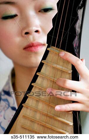 Stock Photography - A young woman playing a Pipa, an ancient style plucked string instrument, Suzhou, Jiangsu Province, China. Fotosearch